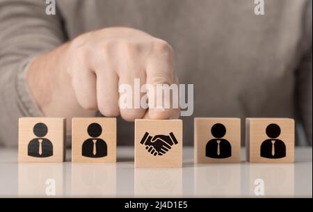 Geschäftsvertrag. Handschüttelns auf einem Holzwürfelblock vor einer menschlichen Ikone für Geschäftsabschlusses und Vertragskonzept. Geschäftliche Kommunikation Stockfoto