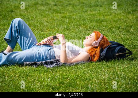 LONDON, GROSSBRITANNIEN. 14 April, 2022 . Eine Frau, die sich bei der warmen Frühlingssonne im Green Park mit Kopfhörern entspannt, während Prognostiker vorhersagen, dass viele Teile des Vereinigten Königreichs über das Osterwochenende schönes Wetter genießen werden.der heißeste Tag des Jahres wird am Karfreitag mit 22celsius erreicht. Kredit: amer ghazzal/Alamy Live Nachrichten Stockfoto