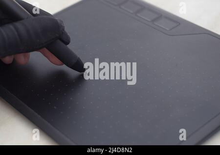 Die Hand des Grafikdesigners in einem schwarzen Handschuh zeichnet auf den Arbeitsbereich eines Grafiktisches Stockfoto