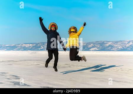 Glückliches Paar springt auf dem gefrorenen Baikalsee. Transparentes Eis. Reisen im Winter, aktive Erholung, Sport. Stockfoto