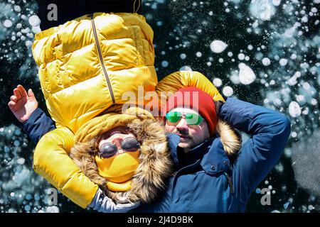 Glückliches Paar liegt auf dem gefrorenen Winter Baikalsee. Transparentes Eis mit Blasen. Reisen im Winter, aktive Erholung, Sport, Urlaub. Stockfoto