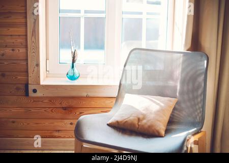 Interieur des gemütlichen modernen Hauses mit ethnischen Boho Dekoration. Sessel mit Kissen auf Holzboden, Vorhänge auf großen Fenstern im rustikalen Wohnzimmer in su Stockfoto