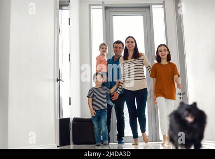 Aufgeregte Kinder, die mit ihren Eltern nach Hause kommen. Kinder nach Hause mit Eltern Mama und Papa, lächelnd niedlichen Kinder Bruder und Schwestern, Eingabe ein Stockfoto