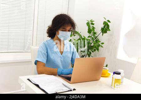 Arzt, der während einer Pandemie an einem Laptop-Computer im Klinikbüro arbeitet. Online-medizinische Beratung Stockfoto