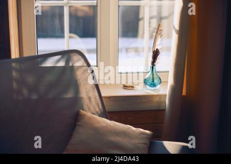 Interieur des gemütlichen modernen Hauses mit ethnischen Boho Dekoration. Sessel mit Kissen auf Holzboden, Vorhänge auf großen Fenstern im rustikalen Wohnzimmer in su Stockfoto