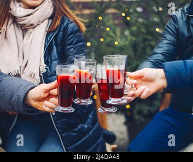 Freunde trinken köstlichen Glühwein auf der Party. Aufnahme einer Gruppe von fröhlichen jungen Freunden, die Spaß haben und ein heißes Getränk auf dem Weihnachtsmarkt genießen Stockfoto