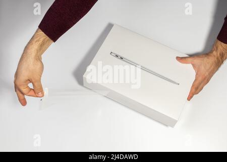 Saratov, Russland - 26. Februar 2022: Halten Sie neue Macbook Air 13 Zoll mit M1 Prozessor in Schutzfolie und Verpackung topview, weißer Hintergrund Stockfoto