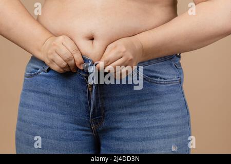 Kaukasische Frau mit großem Bauch und übergewichteten Seiten, die versuchen, blaue Jeans zu zippen. Viszerales Fett. Körper positiv. Plötzliche Gewichtszunahme. Wenig eng Stockfoto