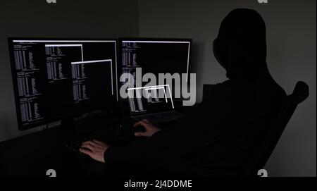 Hacker im Dunkeln arbeiten an mehreren Geräten Stockfoto