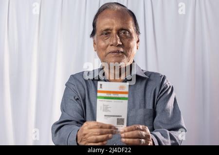 Ein alter indischer Mann, der mit einer Aadhaar-Karte in den Händen auf weißem Hintergrund lächelt Stockfoto