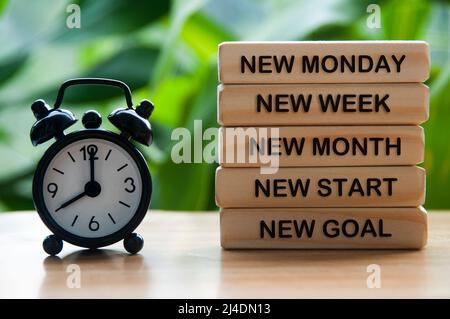 Neuer Text für Montag, Woche, Monat, Start und Ziel auf Holzblock mit Wecker, der auf 8 Uhr zeigt. Konzept für den Neuanfang Stockfoto