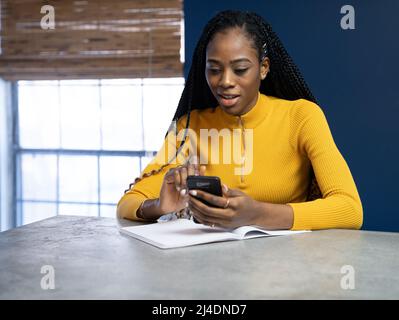 Junge afrikanische amerikanische Schüler mit gelben Hemd an der Theke Insel Schreiben in ein Notebook zu sitzen. Trendy ethnische lifestyle Bild. Stockfoto