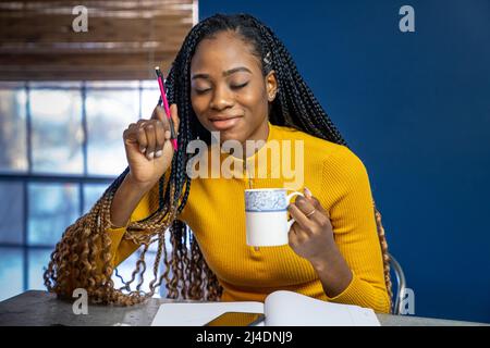 Junge afrikanische amerikanische Schüler mit gelben Hemd an der Theke Insel Schreiben in ein Notebook zu sitzen. Trendy ethnische lifestyle Bild. Stockfoto