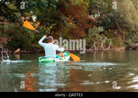 Kajakfahren auf dem Fluss. Erwachsener Mann, der beim Kajak schwimmt. Rückansicht. Speicherplatz kopieren. Das Konzept des Welttourismustages. Stockfoto