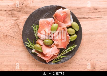 Charcuterie-Tafel mit Proscuitto, serviert mit Oliven auf Holztisch. Schwarzer Teller mit traditionellen italienischen Antipasti. Selektiver Fokus Stockfoto