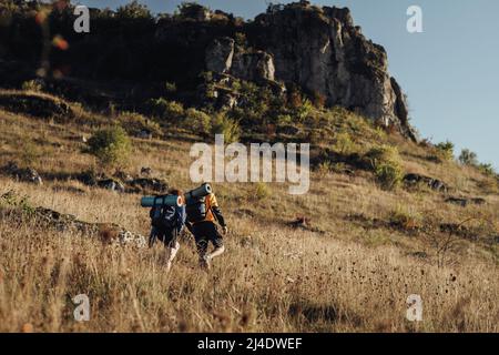 Zwei Wanderer, die während des Sonnenuntergangs auf ihrer Route auf dem Gipfel des Hügels unterwegs sind, genießen einen Wanderausflug Stockfoto