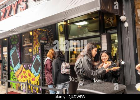 Am Samstag, den 9. April 2022, strömen Menschen zur ZazzyÕs Pizza in der Lower East Side in New York, um an der BackmarketÕs ÒSlices DevicesÓ-Aktion teilzunehmen. Backmarket, ein Wiederverkäufer für gebrauchte Technologien, kauft gebrauchte, in Frage kommende Smartphones und gibt vor Ort Geld ab. Besitzer nicht teilnahmeberechtigter Telefone können sie gegen Pizzastücke und andere Leckereien eintauschen. (© Richard B. Levine) Stockfoto