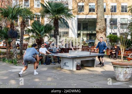 Die Menschen spielen Tischtennis auf dem Londoner Soho Square, wenn das Wetter in Großbritannien, Soho Square, London, Großbritannien eintrifft Stockfoto