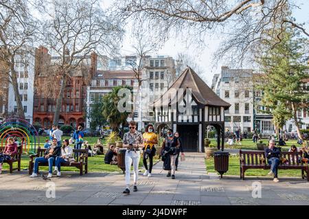 Menschen, die das wärmere Wetter genießen, kommen in Großbritannien, Soho Square, London, Großbritannien an Stockfoto