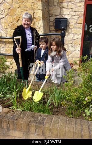 Kirchenminister und zwei Kinder Pflanzen einen Baum zur Feier der Queens Platinum Jubillee 2022 Stratford upon Avon UK Stockfoto