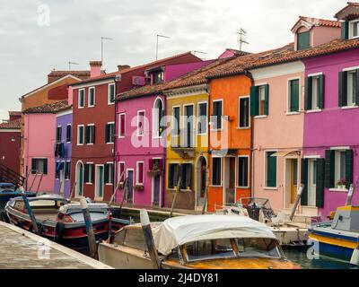 Eine Reihe von bunten Häusern blickt auf den Kanal auf der venezianischen Insel Burano, Boote sind auf dem Kanal vor den Häusern angedockt - Italien Stockfoto