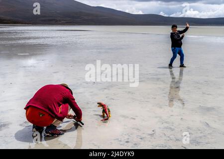 Besucher posieren für Fotos mit Einem Spielzeug-Dinosaurier am Salar de Moche (See Salinas) Salzsee in der Nähe der Stadt Arequipa, Region Arequipa, Peru. Stockfoto