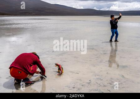 Besucher posieren für Fotos mit Einem Spielzeug-Dinosaurier am Salar de Moche (See Salinas) Salzsee in der Nähe der Stadt Arequipa, Region Arequipa, Peru. Stockfoto