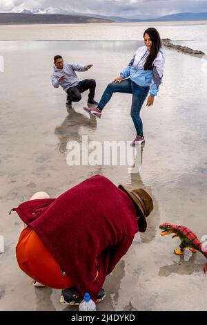 Besucher posieren für Fotos mit Einem Spielzeug-Dinosaurier am Salar de Moche (See Salinas) Salzsee in der Nähe der Stadt Arequipa, Region Arequipa, Peru. Stockfoto