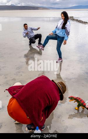 Besucher posieren für Fotos mit Einem Spielzeug-Dinosaurier am Salar de Moche (See Salinas) Salzsee in der Nähe der Stadt Arequipa, Region Arequipa, Peru. Stockfoto