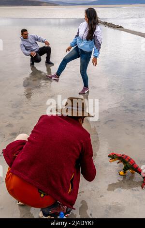 Besucher posieren für Fotos mit Einem Spielzeug-Dinosaurier am Salar de Moche (See Salinas) Salzsee in der Nähe der Stadt Arequipa, Region Arequipa, Peru. Stockfoto