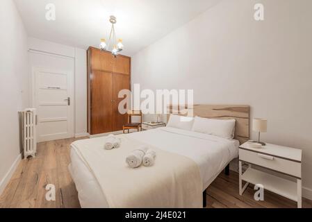 Schlafzimmer mit Doppelbett mit Rollhandtüchern und Einbauschrank mit Holztüren und einteiligem Kofferraum, einteiligem Kopfteil aus Holz und zwei weißen Einzelbetten Stockfoto