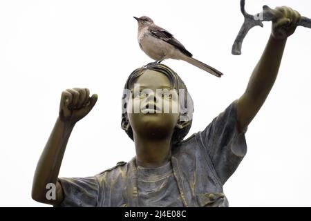 Bronzestatue eines Jungen mit einem lebenden Vogel, der auf dem Kopf des Kindes im Lilburn Park in Metro Atlanta, Georgia, steht. (USA) Stockfoto