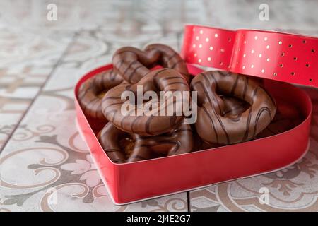 Valentinstag-Kekse. Mit Schokolade beschichtete Lebkuchenkekse. In einer roten herzförmigen Schachtel. Stockfoto