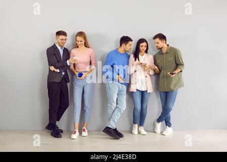Eine Gruppe junger Männer und Frauen, die im Büro stehen und ihre Mobiltelefone gemeinsam nutzen Stockfoto