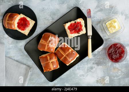 Frisch gebackene, heiße Brötchen mit Himbeermarmelade und Butter auf schwarzen, matten Tellern, die von oben geschossen wurden. Traditionelle Oster-Backwaren. Stockfoto