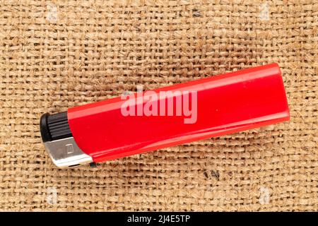Ein rotes Feuerzeug auf Jute-Stoff, Makro, Draufsicht. Stockfoto