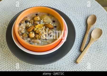 Traditionelles türkisches Dessert Ashure oder Noah's Pudding in stilvoller Schale auf weißer Oberfläche mit Holzlöffel.Türkische Küche Stockfoto