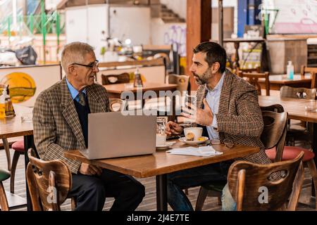 Zwei ältere Geschäftsleute sprechen, während sie im Café sitzen Stockfoto