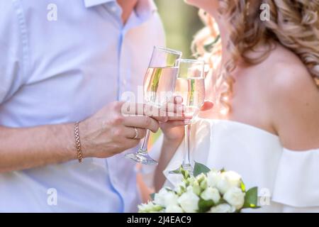 Zwei Gläser Sekt in der Hand, ein Konzept für einen Urlaub, Bokeh, im Restaurant oder im Freien. Damen- und Herrenhände halten eine Champagnerglasse Stockfoto