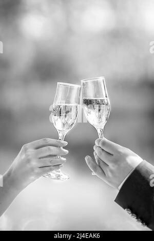 Zwei Gläser Sekt in der Hand, ein Konzept für einen Urlaub, Bokeh, im Restaurant oder im Freien. Damen- und Herrenhände halten eine Champagnerglasse Stockfoto