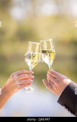 Zwei Gläser Sekt in der Hand, ein Konzept für einen Urlaub, Bokeh, im Restaurant oder im Freien. Damen- und Herrenhände halten ein Sektglas Stockfoto