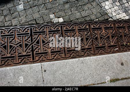 Gusseisernes Gitter über dem Abfluss. Gusseisernes Gitter über dem Ablaufkanal. Sturmwasser-Ablaufgrill auf einem Steinsteig. Stockfoto