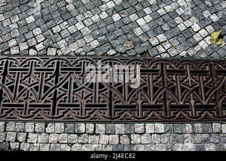 Gusseisernes Gitter über dem Abfluss. Gusseisernes Gitter über dem Ablaufkanal. Sturmwasser-Ablaufgrill auf einem Steinsteig. Stockfoto