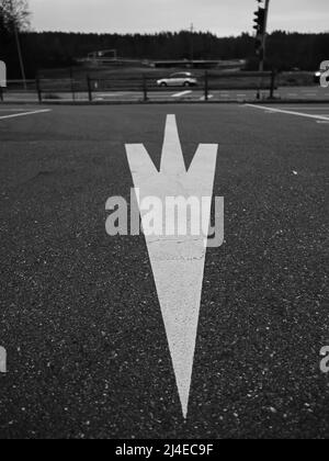 Monochromes Bild eines großen weißen Pfeils auf dem Boden eines Parkplatzes Stockfoto