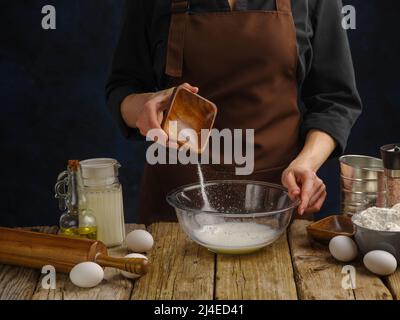 Kochen von Teig in einer Glasschüssel auf einem hölzernen Küchentisch durch die Hände eines professionellen Küchenchefs. Viele Zutaten. Hausmannskost, Restaurant, Hotel, foo Stockfoto