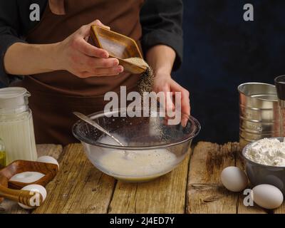 Nahaufnahme. Der Koch bereitet den Teig in einer großen Glasschüssel auf einem hölzernen Küchentisch zu. Das Konzept ist Rezepte für die Zubereitung von Gerichten aus Teig - Pasta, Stockfoto