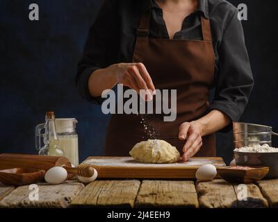 Kochen Teig durch den Koch in einem Restaurant, Hotel, Hausküche. Dunkelblauer Hintergrund. Zutaten auf einem hölzernen Küchentisch. Rezeptbuch, Food Blog, s Stockfoto