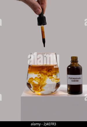 Jodidtabletten flüssig für den Einsatz bei radioaktiver Kontamination. Eine Hand tropft von einer Pipette in ein Glas Wasser. Der Name des Arzneimittels Stockfoto