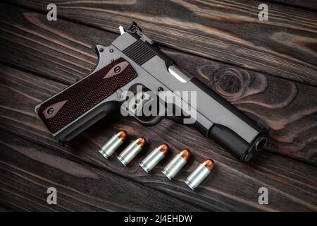 Moderne schwarze Pistole und Munitionskunition auf einem hölzernen Hintergrund. Pistole. Waffen für Sport und Selbstverteidigung liegen auf dem Tisch. Stockfoto