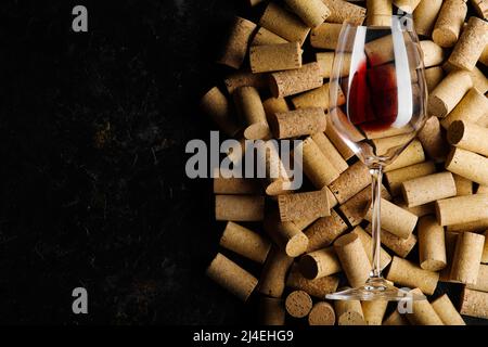 Rotwein im Glas und viele Weinkorken. Isoliert auf schwarzem Hintergrund. Weinprobe, Weinsammlung, Feier, Bankett. Restaurant, Hotel. Erw Stockfoto